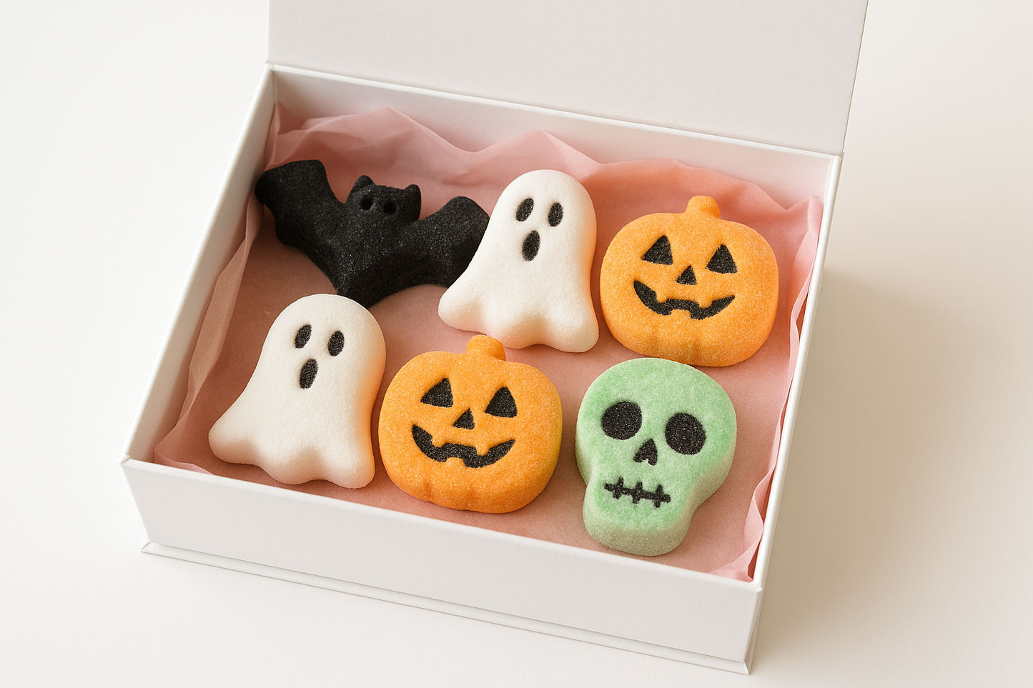 kan du göra en bild på en vit gift box med rosa gift papper under som innehåller 6 st marsmellos 1. fläddermoss svart , 2. gost vit 3. pumpkin ansikte orange 4. dödskalle grön blandad med vit bakgrund