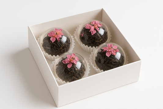 kan du göra en bild på en vit gift box med 4 genomskinliga te bomb som innehåller svart te och designade med rosa torkade blommor med vit bakgrund