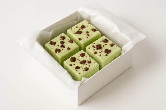 kan-du-g-ra-en-bild-p-en vit gift box med vit gift papper och 4-mellan-stora-fyrkantigt-pistage-gr-n-marsmello-med-choklad-bitar-p-och-vit-background